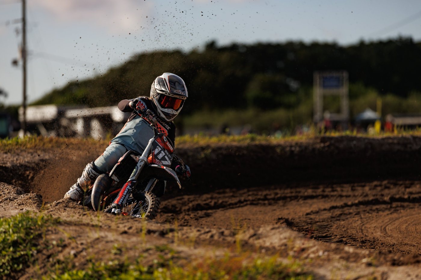 Young motocross rider leaning into a sandy berm with dirt flying behind the bike